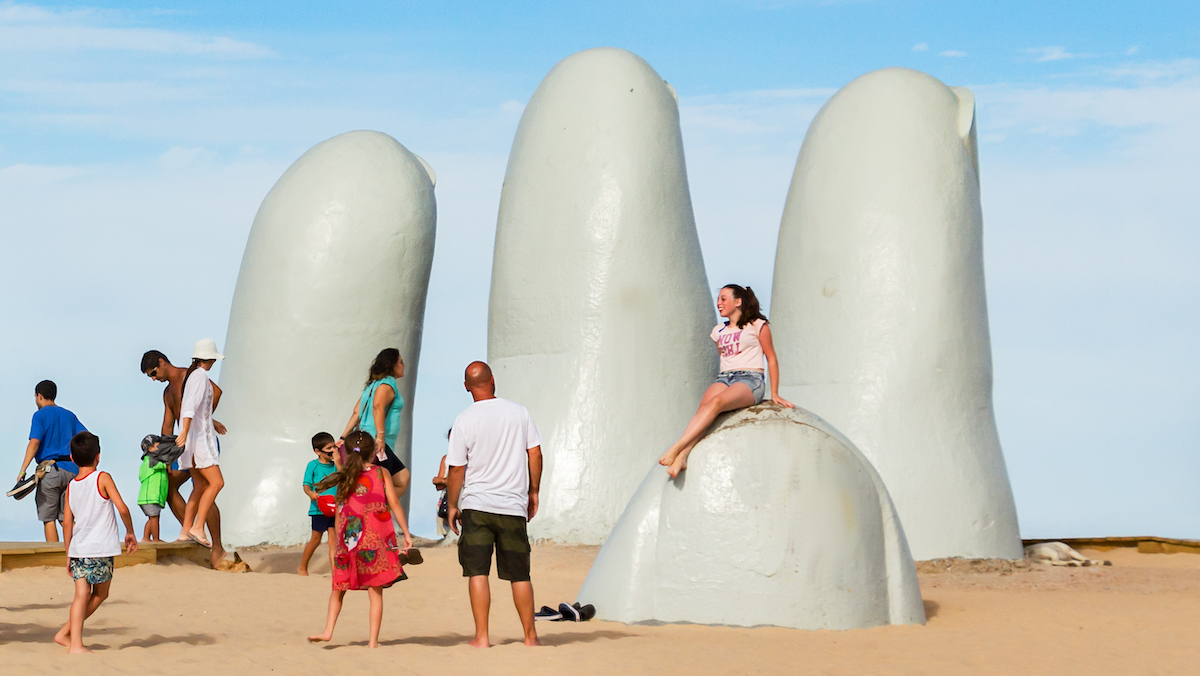 people in uruguay at a sculpture of fingers coming out of sand